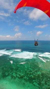 FPV drone shot of paragliders gliding over turquoise ocean and cliffs in Bali, Indonesia