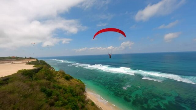 FPV drone shot of paragliders gliding over turquoise ocean and cliffs in Bali, Indonesia