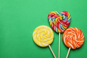 Tasty lollipops on green background, flat lay. Space for text