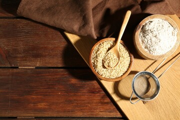 Brown rice, flour and sieve on wooden table, flat lay. Space for text