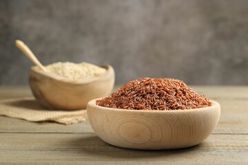 Raw brown rice in bowl on wooden table against grey background, closeup