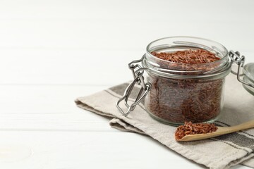 Raw brown rice in open jar and spoon on white wooden table, closeup. Space for text