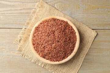 Raw brown rice in bowl on wooden table, top view