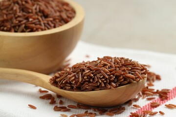 Brown rice in wooden spoon and bowl on table, closeup