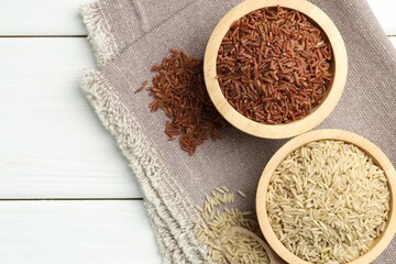 Different types of brown rice in bowls and scoop on white wooden table, flat lay. Space for text