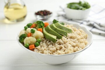 Tasty brown rice with vegetables in bowl on white wooden table, closeup