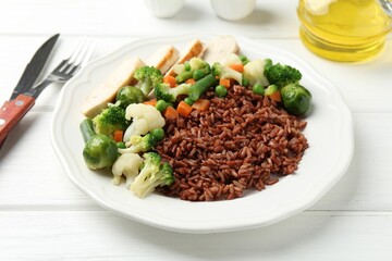 Tasty brown rice with vegetables and chicken on white wooden table, closeup