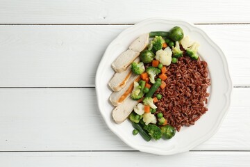 Tasty brown rice with vegetables and chicken on white wooden table, top view. Space for text
