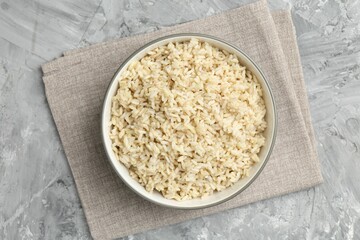 Delicious brown rice served on grey textured table, top view
