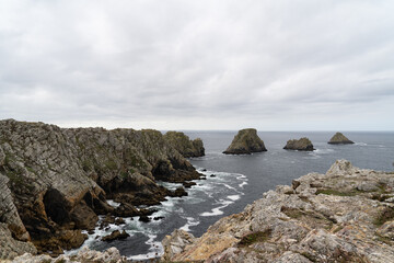 Le Tas de Pois sous un ciel couvert, les vagues se brisant contre les rochers sculptent une écume blanche tourbillonnante, contrastant avec les teintes sombres de la mer d'Iroise.