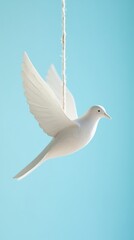 Fototapeta premium A close-up of a single paper dove hanging against a soft blue sky. Sunlight highlights its edges, creating a minimalistic, peaceful, and elegant mood.