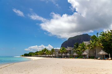 Tropical paradise beach resort with thatched umbrellas and loungers under trees.Idyllic beach resort with palm-thatched cabanas along white sandy shoreline