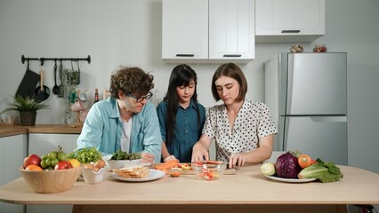 Happy father move to music while cooking food and prepare lunch at modern kitchen. Active dad dancing to song while making healthy food or salad surrounded with vegetable and kitchenware. Pedagogy.
