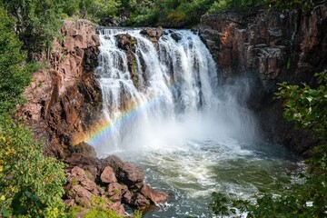 Fototapeta premium Scenic waterfall with rainbow in lush green landscape