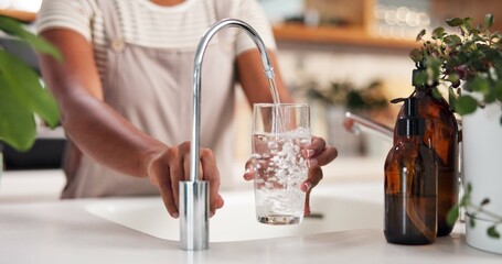 Hands, glass and water by faucet in kitchen for hydration, thirst or wellness in morning at...
