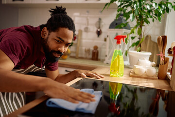 Black man cleaning electric ceramic stove in kitchen.