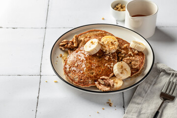 Healthy oatmeal pancakes with banana, nuts and honey on white tile background, text space. Morning food breakfast. Pancake day or Maslenitsa recipe