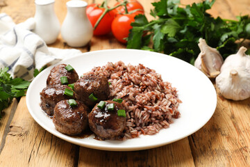 Tasty meatballs with sauce, brown rice and green onion on wooden table, closeup