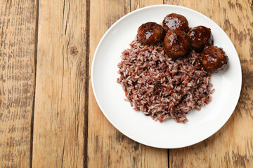 Tasty meatballs with sauce and brown rice on wooden table, top view. Space for text