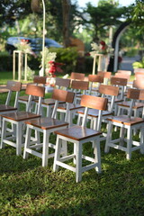 A row of brown wooden chairs with white legs neatly arranged on green grass, seemingly prepared for...
