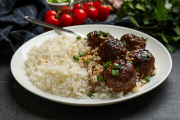 Delicious rice with meatballs, sauce and green onions on black table, closeup