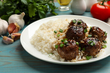 Delicious rice with meatballs, sauce and green onions on blue wooden table, closeup