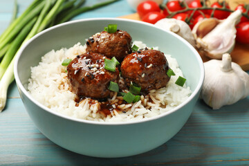 Delicious rice with meatballs, sauce and green onions on blue wooden table, closeup