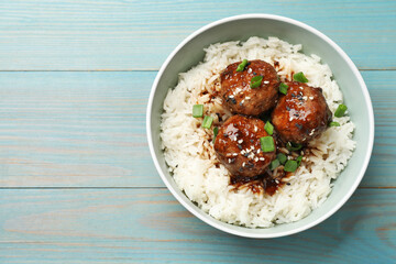 Delicious rice with meatballs, sauce and green onions in bowl on blue wooden table, top view. Space for text