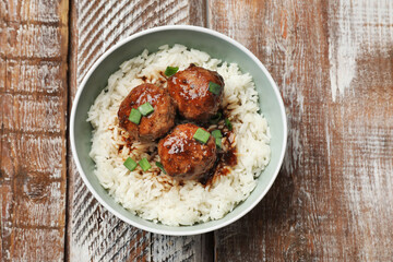 Delicious rice with meatballs, sauce and green onions in bowl on wooden table, top view