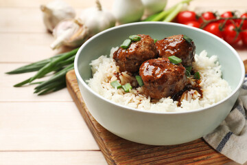 Delicious rice with meatballs, sauce and green onions on white wooden table, closeup