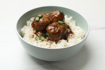 Delicious rice with meatballs, sauce and green onions in bowl on white marble table, closeup
