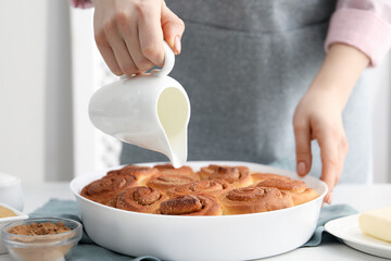 Woman with freshly baked cinnamon rolls and pitcher at white table indoors, closeup
