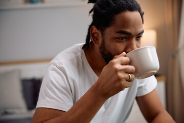 Black man having cup of coffee in bedroom in morning.