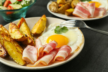 Tasty brunch. Fried egg, potato, bacon and fork on dark textured table, closeup