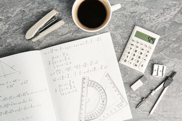 Doing homework. Notebook with math assignment, coffee and stationery on grey desk, flat lay
