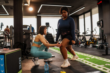 Determined overweight woman performing lunges with dumbbells, guided by her personal trainer,...