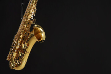Fototapeta premium Jazz. One beautiful saxophone hanging from strap on black background, space for text