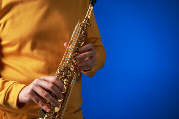 Professional musician with soprano saxophone on blue background, closeup. Space for text