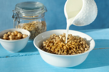 Pouring milk into bowl with oatmeal at light blue wooden table, closeup