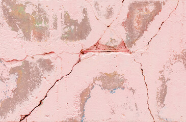 Close-up of a cracked pink stucco wall showing layers of other colors underneath,signs of erosion and deterioration creating an abstract textured background,