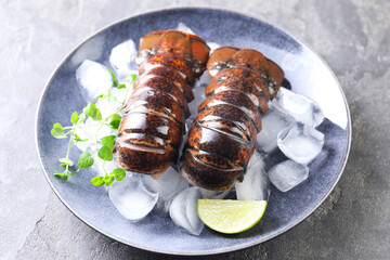 Raw lobster tails with microgreens, lime and ice on grey table, closeup
