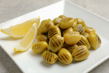 Grilled green olives and lemon wedges on gray table, closeup
