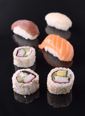 Sushi rolls and nigiri resting on reflective black surface
