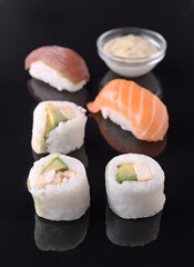 Delicious sushi assortment with salmon, tuna, and avocado rolls on black reflective surface