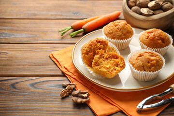 Tasty carrot muffins, fresh vegetables, nutcracker and walnuts on wooden table, closeup. Space for...