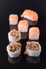 Delicious sushi pieces with salmon and crispy onions on black reflective surface