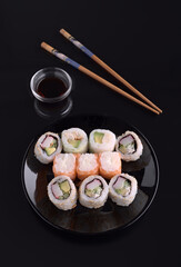 Delicious sushi rolls with soy sauce and chopsticks on black background