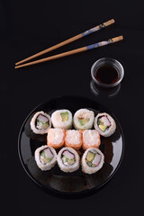 Sushi rolls with soy sauce and chopsticks on black background