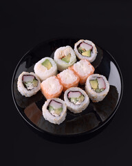 Variety of sushi rolls presented on black plate with black background