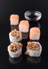 Delicious sushi rolls with salmon and crispy onions on black reflective surface with soy sauce